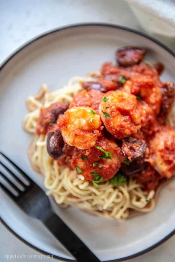 a plate of garlic shrimp with puttanesca sauce atop a marble table top