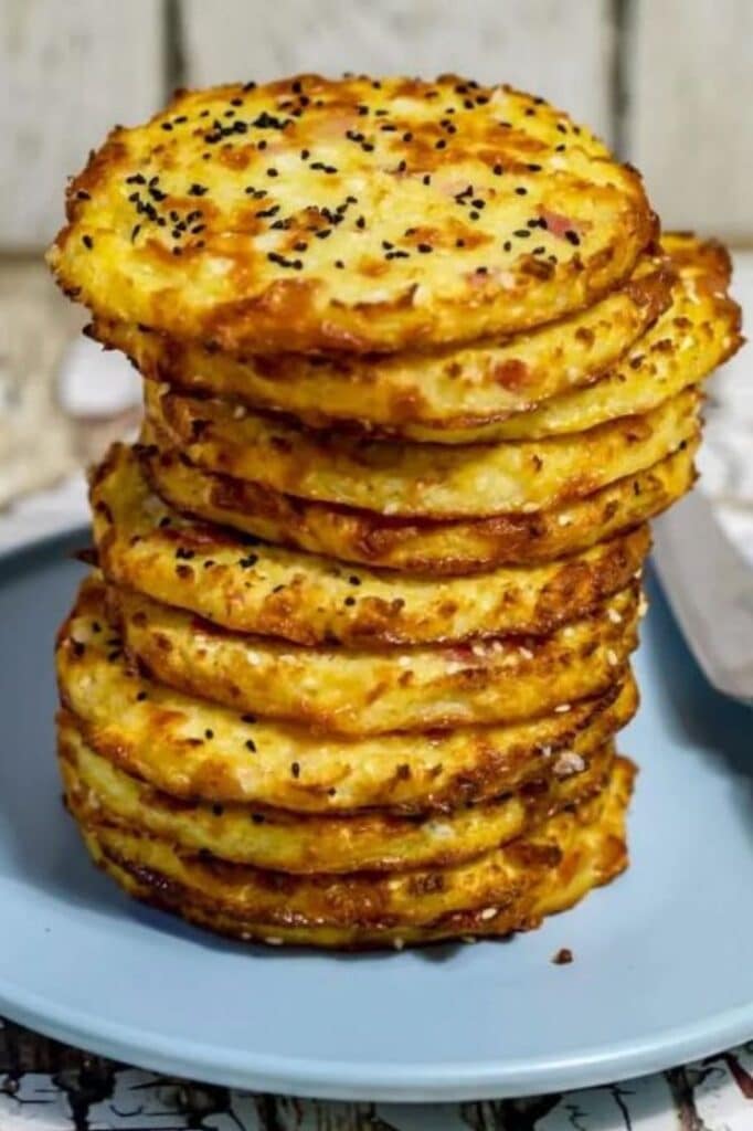 a stack of keto cheese and bacon cauliflower buns on a blue plate atop a wooden table