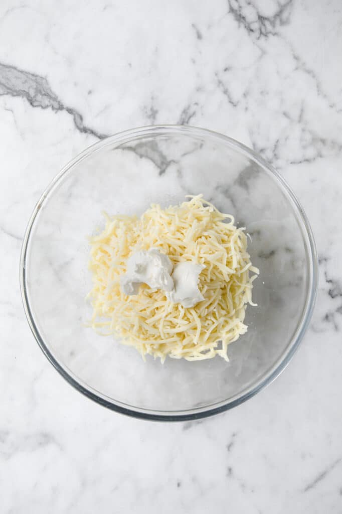 shredded mozzarella cheese in a microwaveable mixing bowl atop a marble kitchen counter