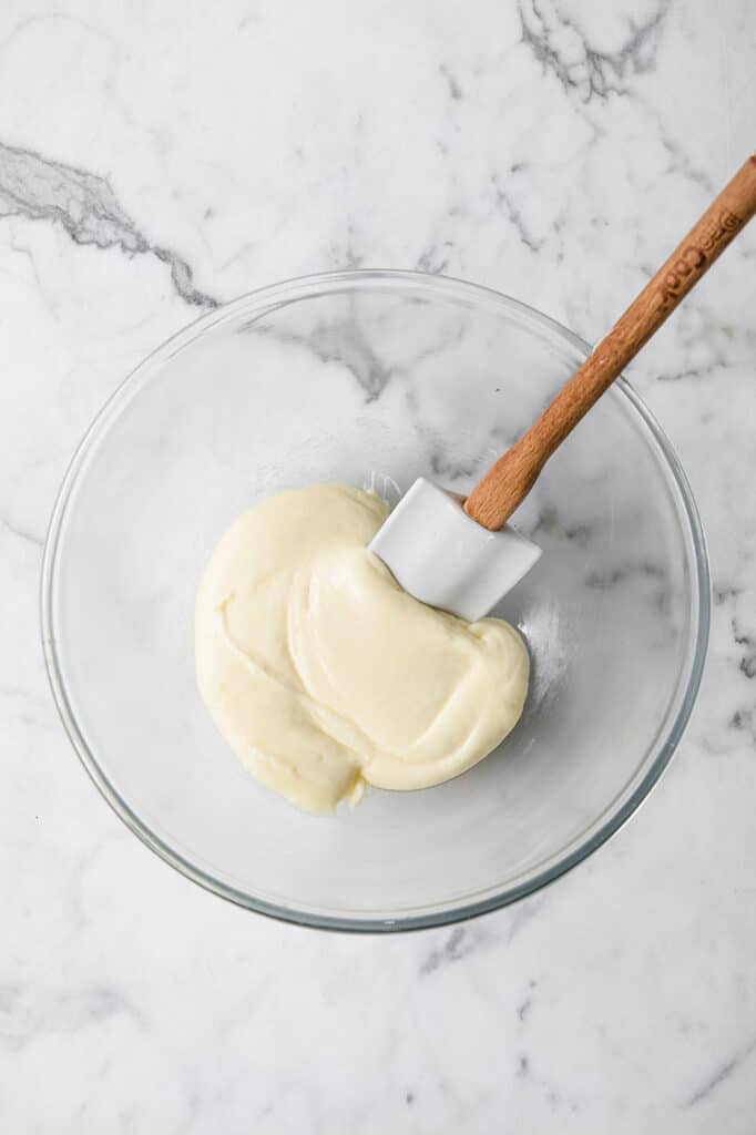 melted mozzarella cheese being mixed with a spatula in a glass mixing bowl atop a marble kitchen counter