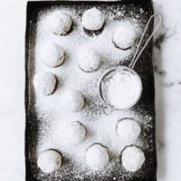 nut-free keto snowball cookies being dusted by powdered sweetener on a baking tray atop a marble kitchen counter