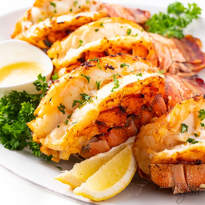 a plate of broiled lobster tail garnished with lemons and herbs atop a marble table