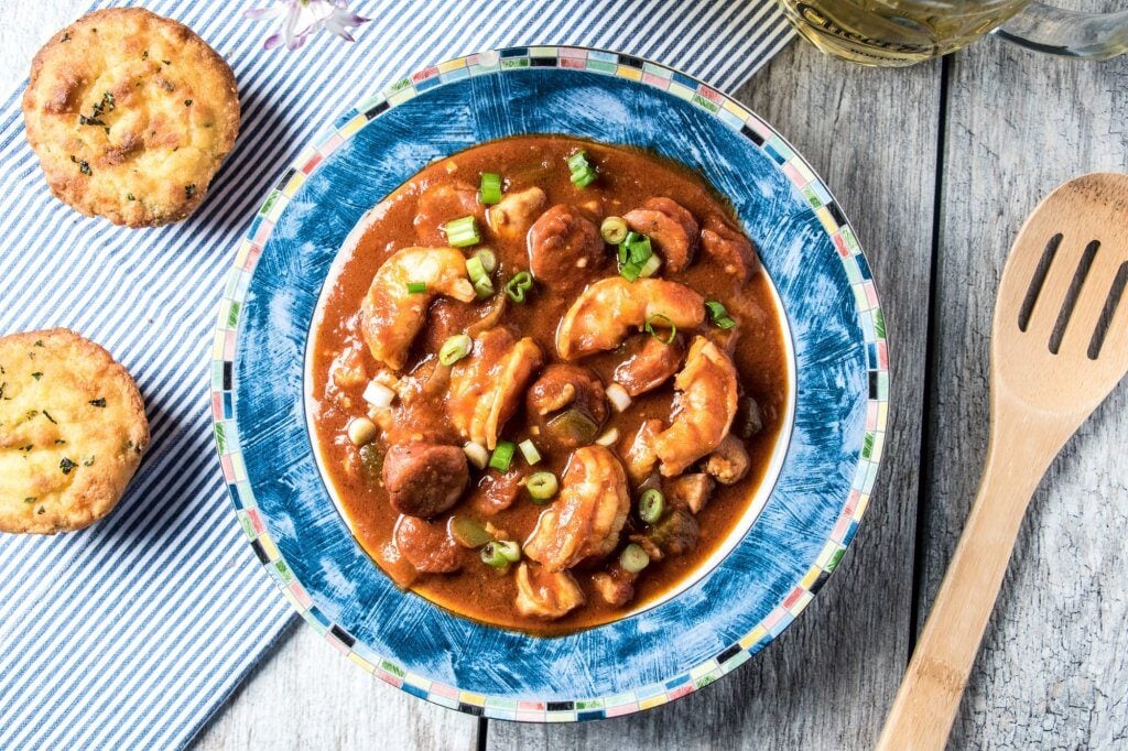 a bowl of keto chicken shrimp gumbo with sausage garnished with spices atop a wooden table
