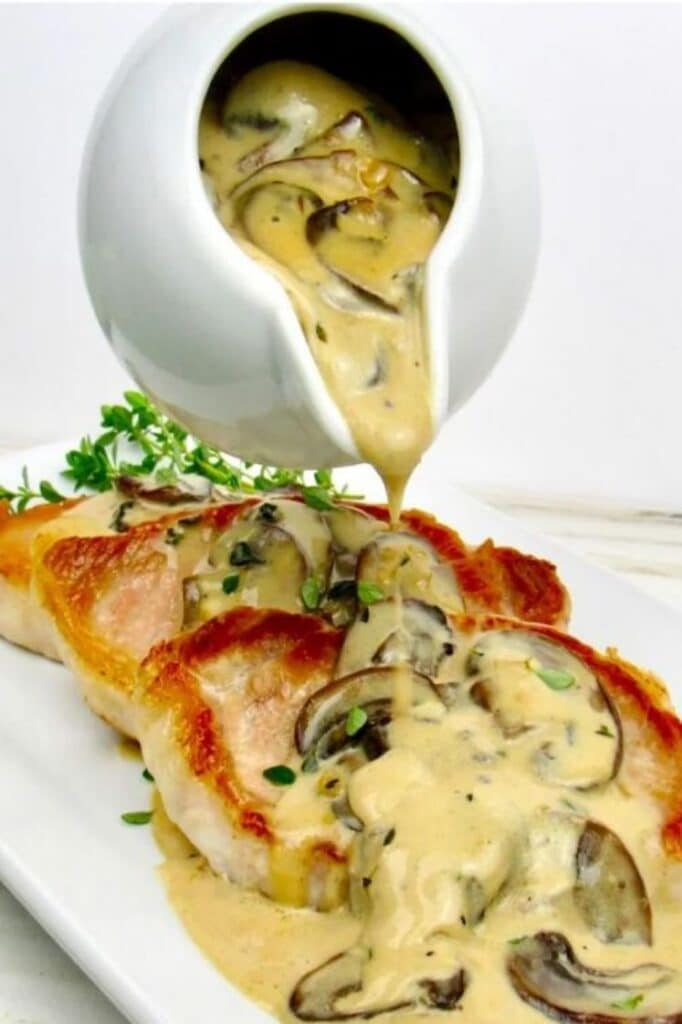 creamy mushroom gravy being poured on three slices of pork chop on a plate atop a marble kitchen table