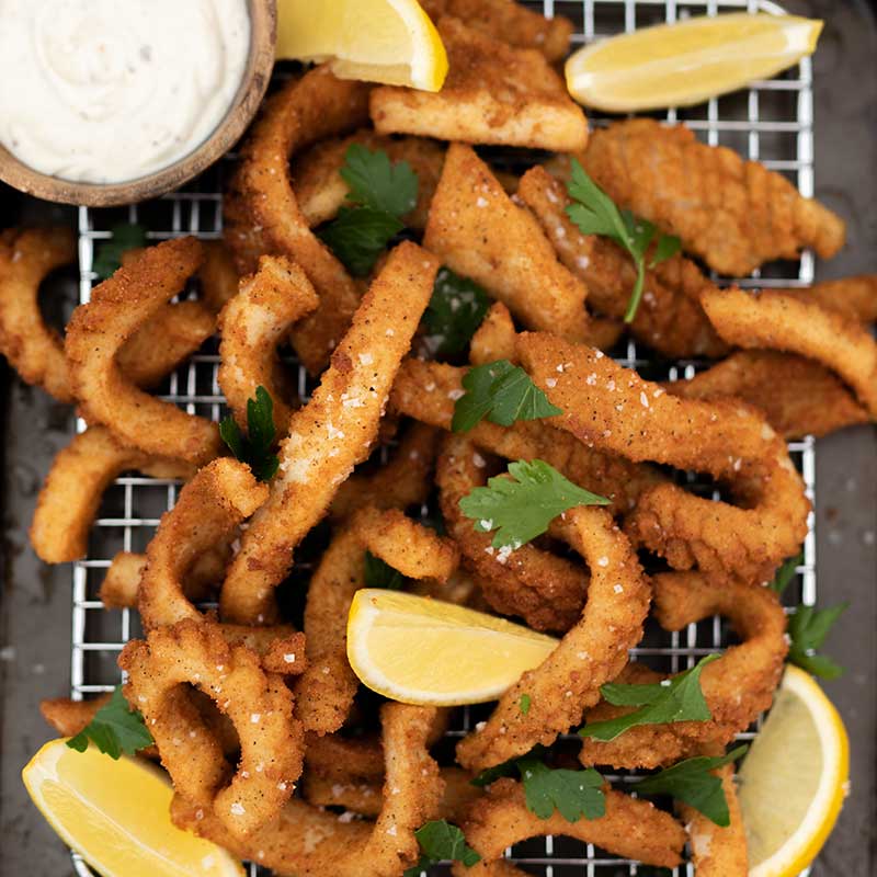 keto salt & pepper squid resting on a wire rack garnished with slices of lemons