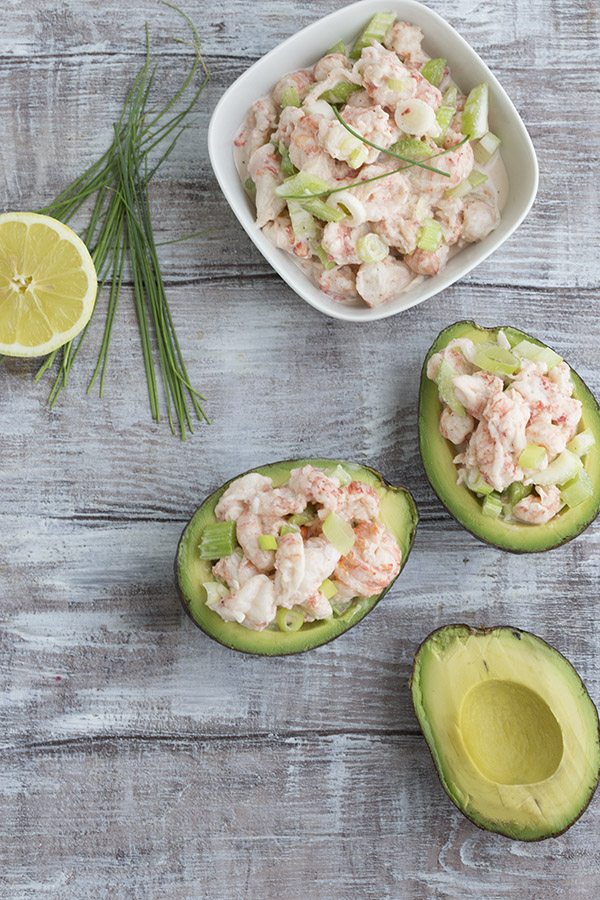 3 avocadoes sliced in half topped with lobster rolls atop a wooden table