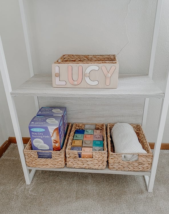 white bookshelf holding bins with baby items inside for girl nursery