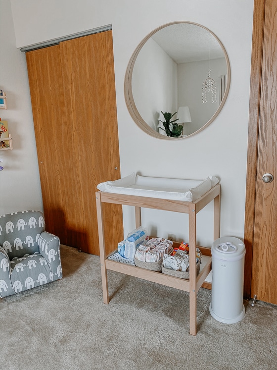wooden diaper changing station with diaper pad and diapers and diaper pail with mirror hanging overhead