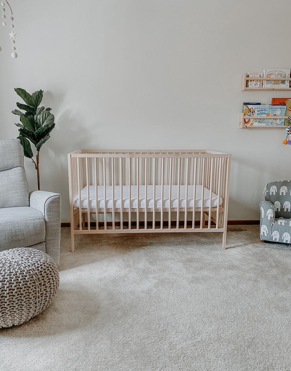 wooden ikea crib in nursery with glider and pouf and fake plant