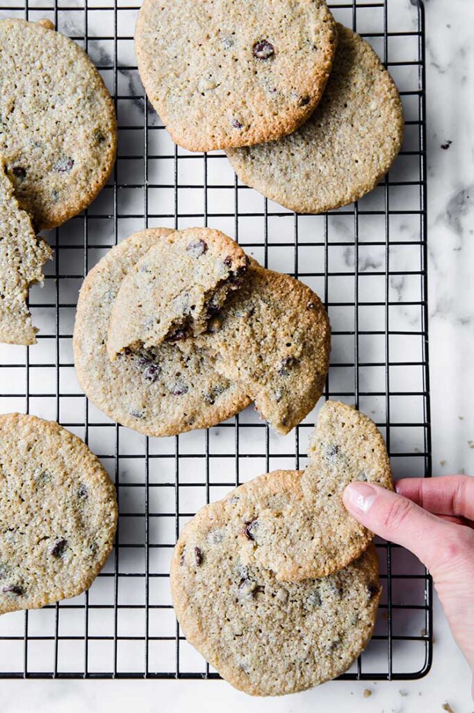 nut-free keto chocolate cookie broken in half being picked up by hand on a wire rack atop a marble kitchen coutner