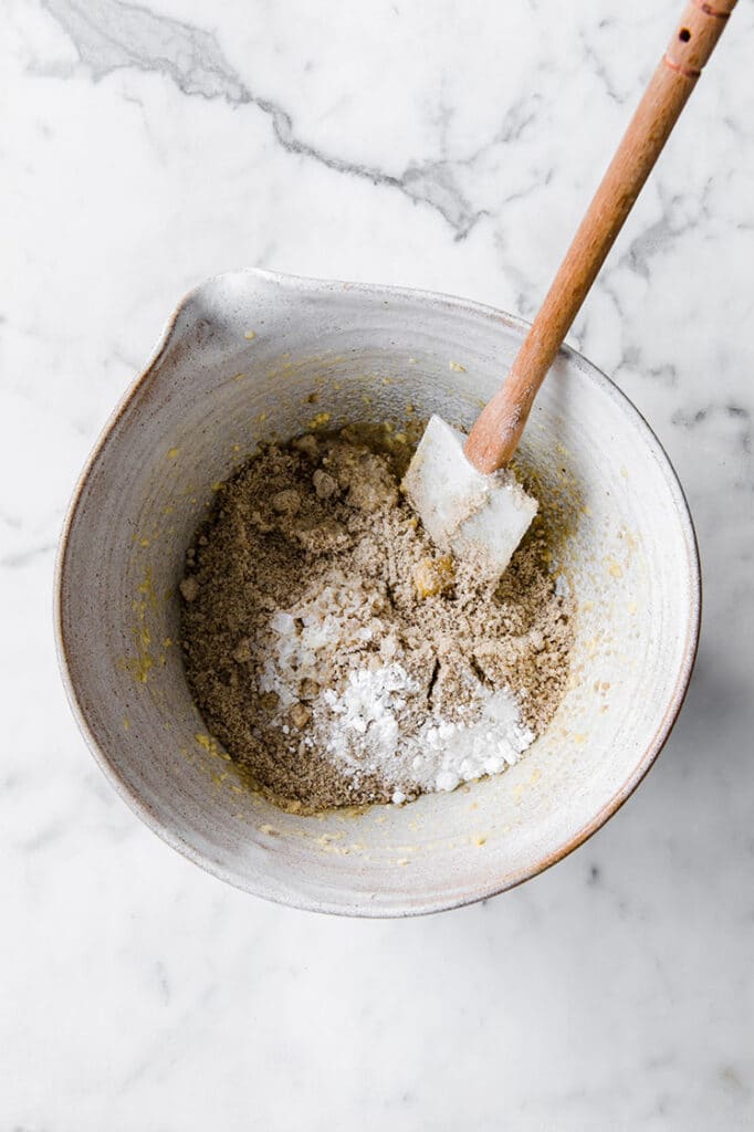 dry chocolate cookie dough ingredients added on top of wet cookie dough ingredients in a large mixing bowl atop a marble kitchen table