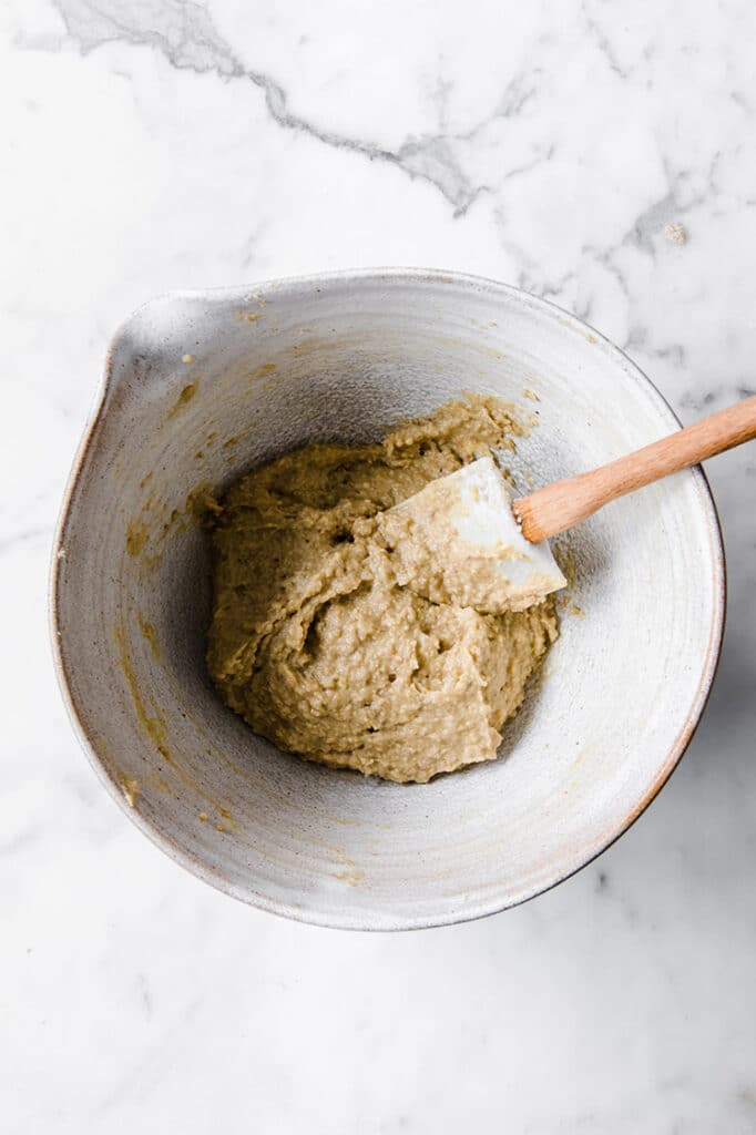 nut-free chocolate chip cookie dough being mixed with a spatula in a large mixing bowl atop a marble kitchen table