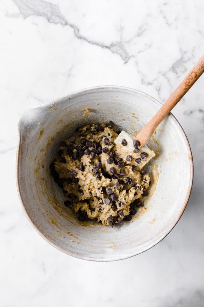chocolate chips added on top of cookie dough in a large mixing bowl atop marble kitchen table
