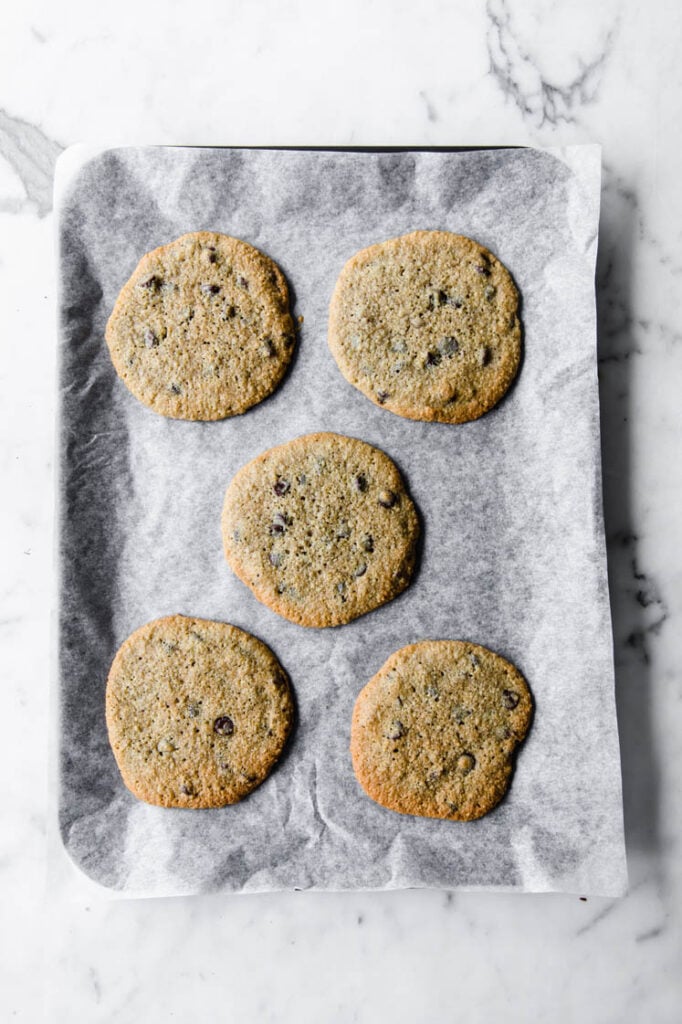 5 nut-free chocolate chip cookies on a baking sheet lined with parchment paper atop a marble kitchen table