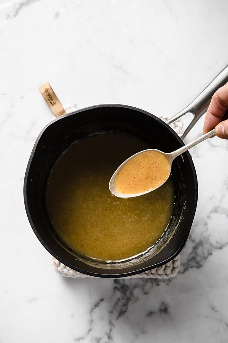 melted caramel in a saucepan scooped by a spoon atop a marble kitchen counter