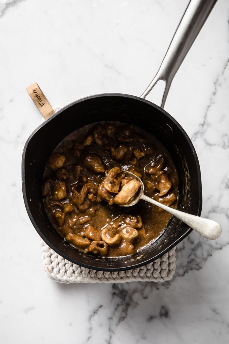 pork rinds added in a saucepan of melted caramel atop a marble kitchen counter