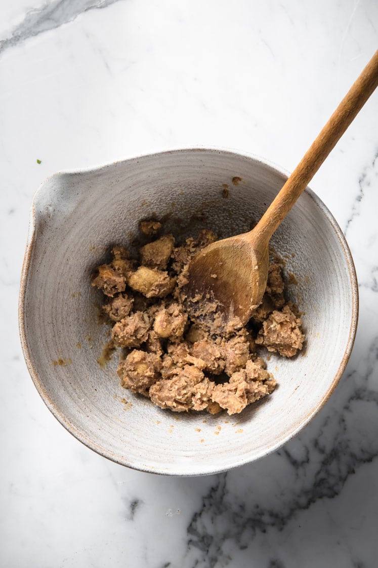 a bowl of cinnamon toast crunch cereal being stirred by a wooden spatula atop a marble kitchen counter