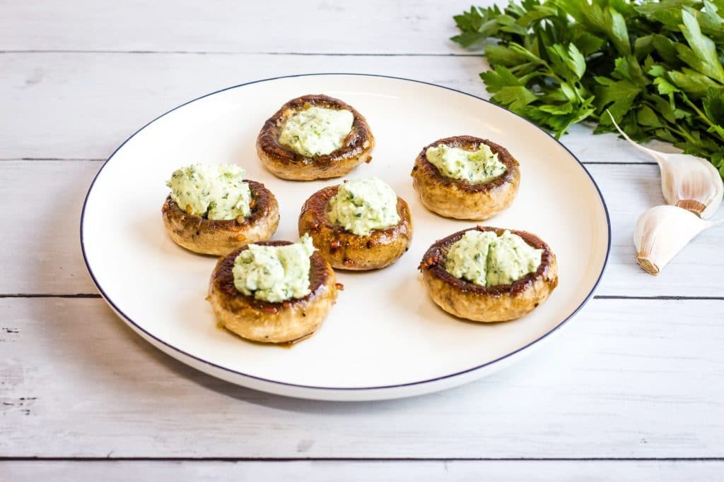 five green goddess stuffed mushrooms on a plate atop a wooden table