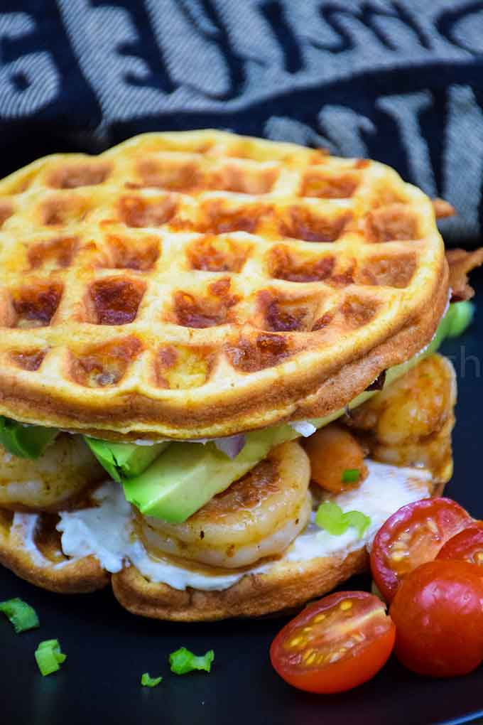 cajun shrimp and avocado chaffle sandwich on a plate garnished with cherry tomatoes