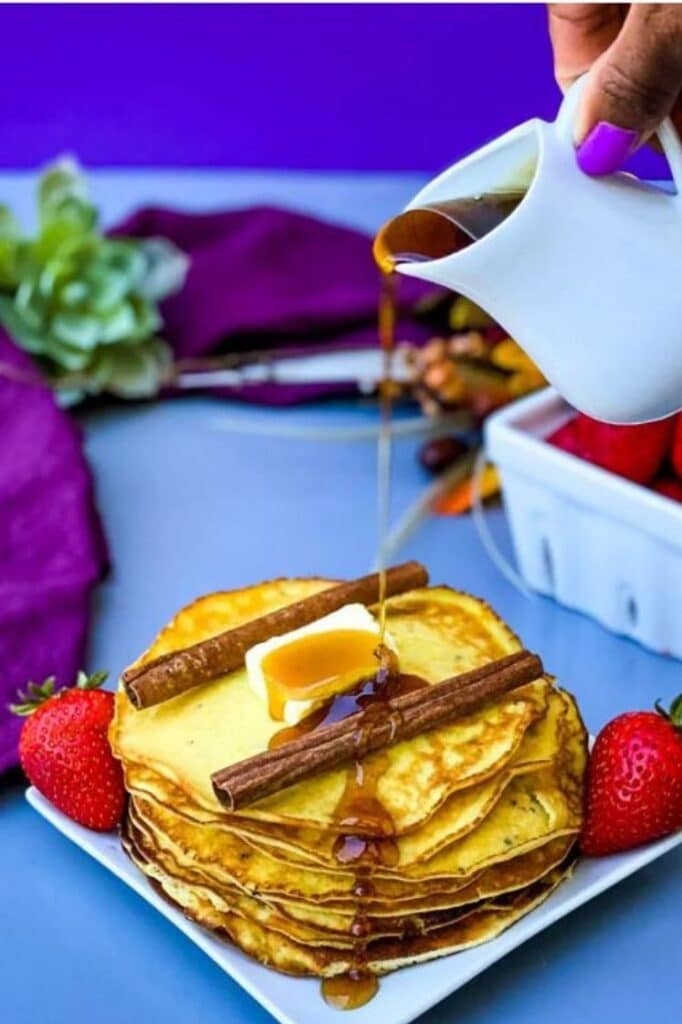 syrup being poured on top of cream cheese pancakes on a plate atop a blue table