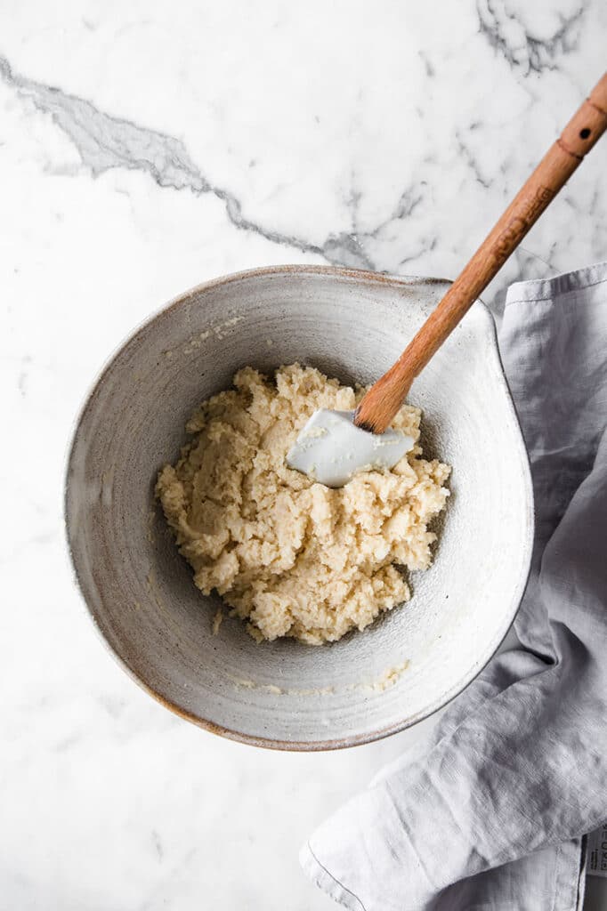 a well mixed low carb coconut blondies dough in a bowl with a rubber spatula. atop a marble kitchen table