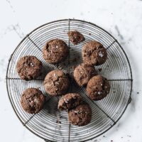 Close-up shot of nut-free keto chocolate sea salt cookies resting on a baking rack, atop a marble countertop.