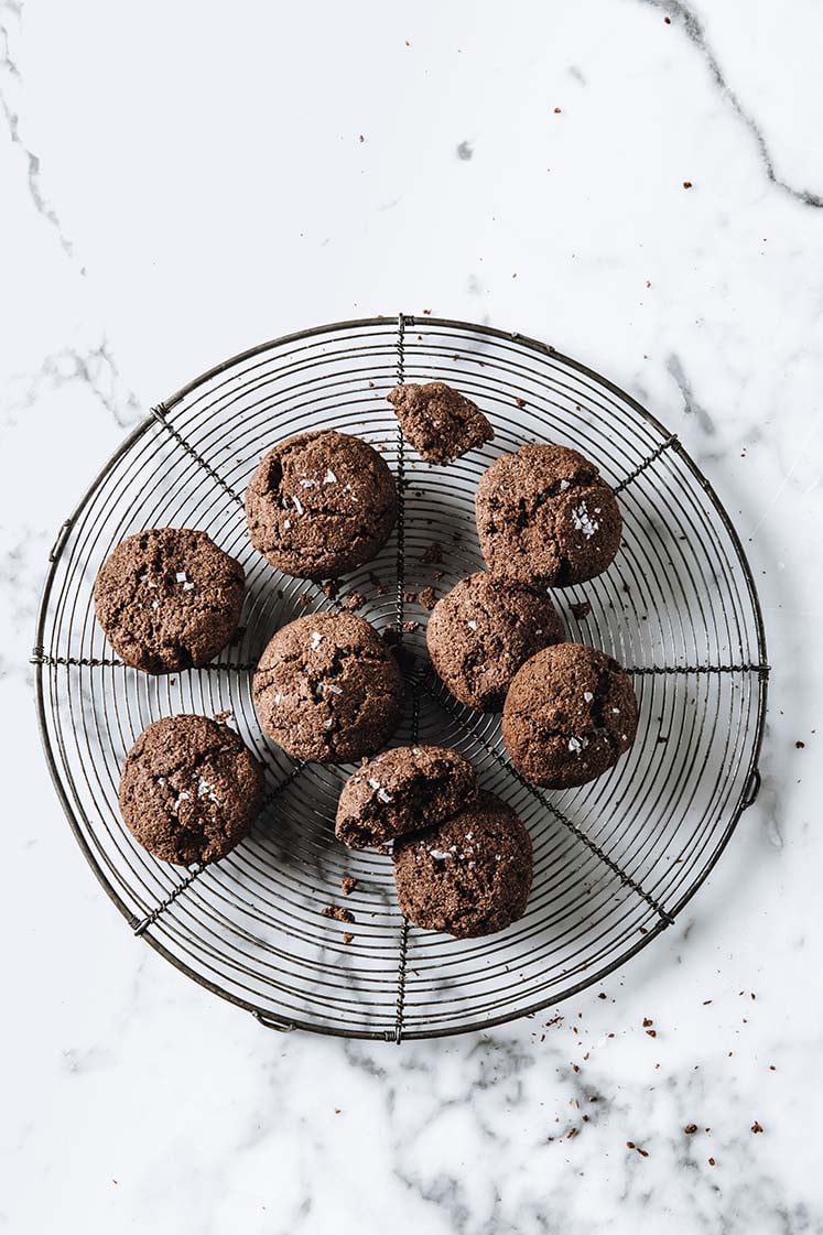 Close-up shot of nut-free keto chocolate sea salt cookies resting on a baking rack, atop a marble countertop.