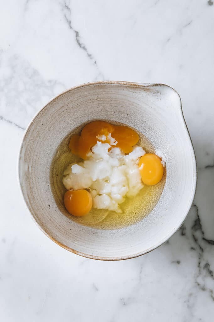 coconut oil, eggs and vanilla extract in a bowl atop a marble kitchen table