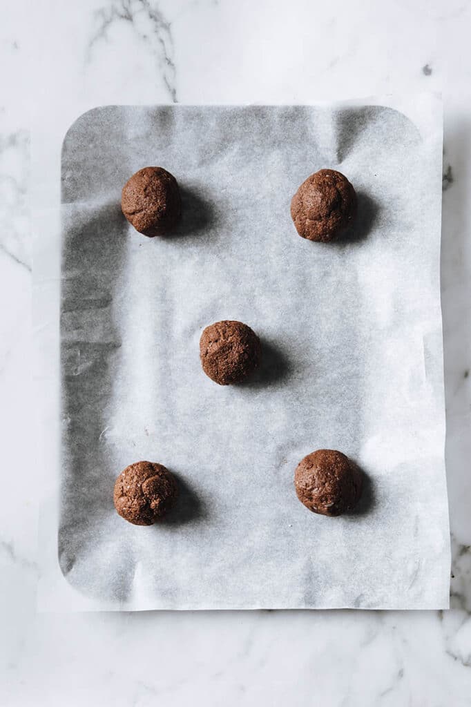 keto chocolate sea salt cookie dough rolled into 5 balls on a parchment paper lined baking sheet atop a marble kitchen counter