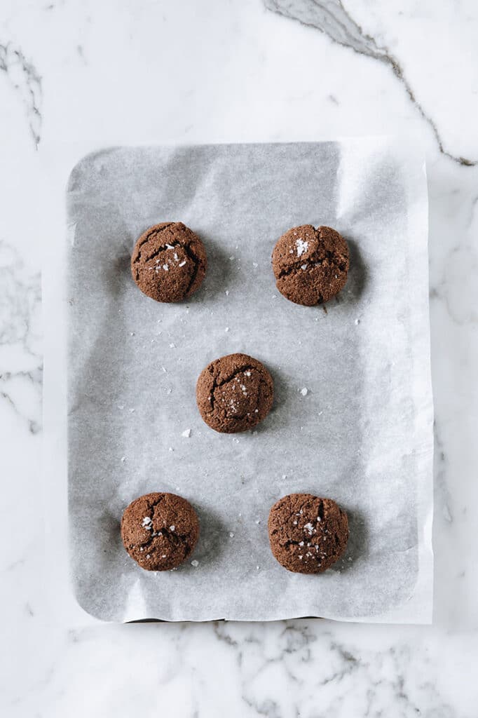 5 baked keto chocolate sea salt cookies on parchment paper lined baking sheet atop a marble kitchen counter