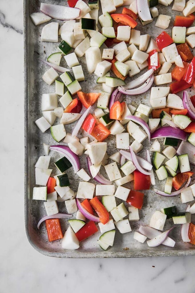 chopped turnips, red pepper, onion, and zucchini on a baking tray atop a marble kitchen counter.