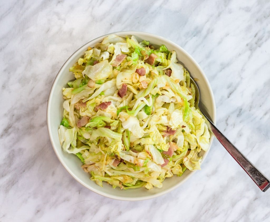 a bowl of skillet cabbage with bacon & garlic atop a table