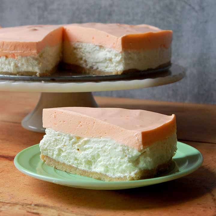 a slice of orange creamsicle cheesecake with a whole cake on the background atop a wooden table