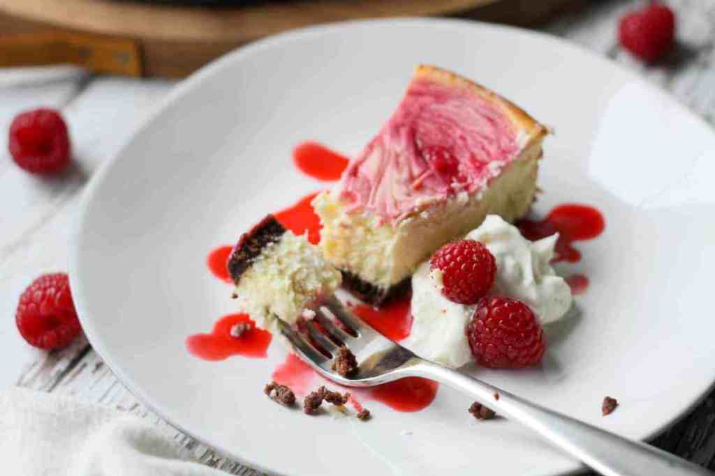 a slice of sugar-free white chocolate raspberry cheesecake on a plate topped with cream and berries