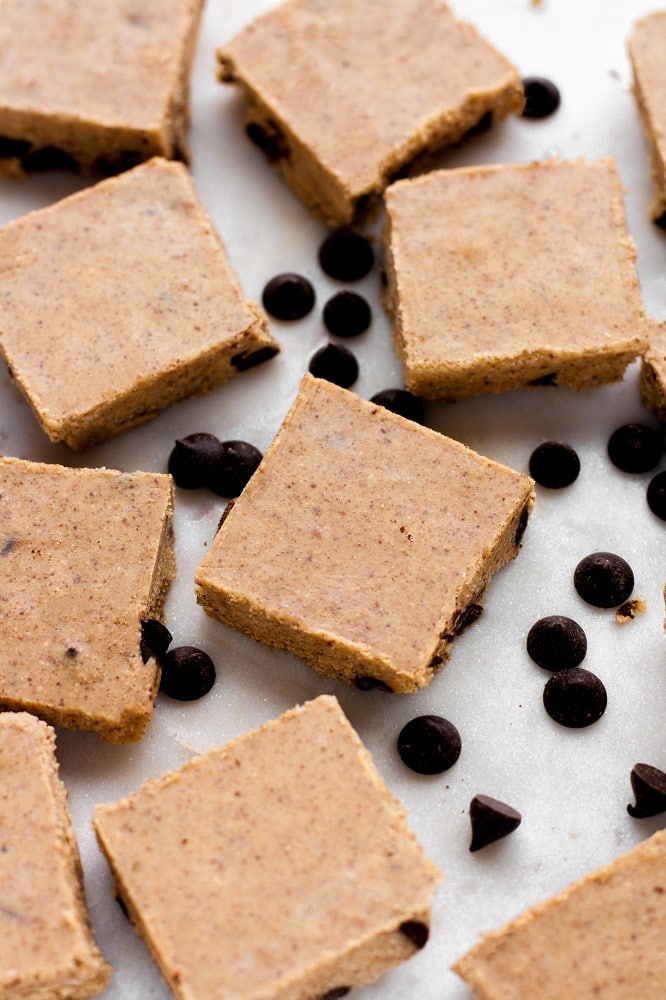 side-angle-shot-of-no-bake-chocolate-chip-almond-butter-fat-bomb-bars-surrounded-by-pascha-chocolate-chips