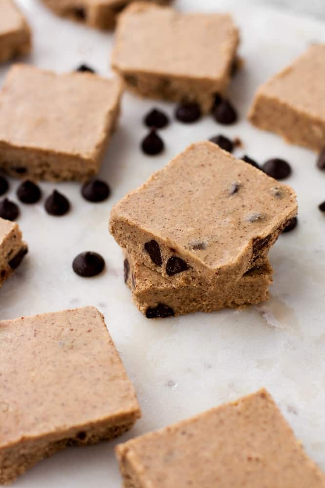 side-angle-shot-of-stack-of-no-bake-chocolate-chip-almond-butter-fat-bomb-bars-surrounded-by-pascha-chocolate-chips