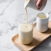 keto nut-free sweetened condensed milk being poured on a glas jar atop a marble kitchen table