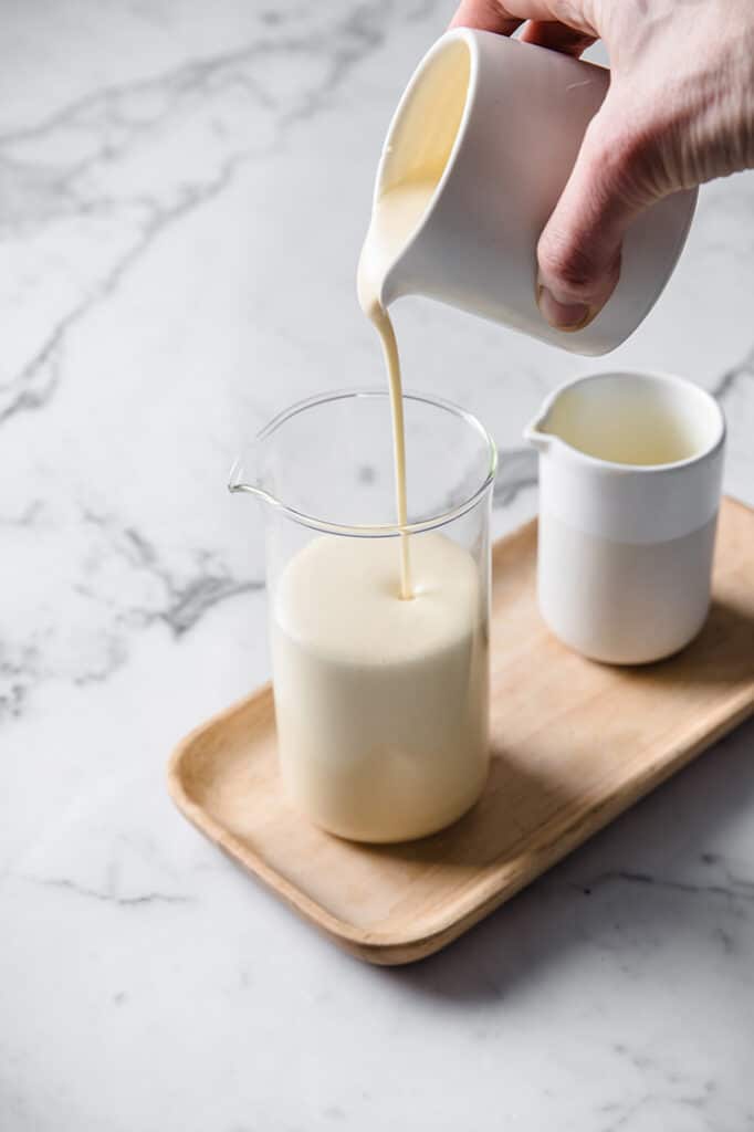 keto nut-free sweetened condensed milk being poured on a glas jar atop a marble kitchen table