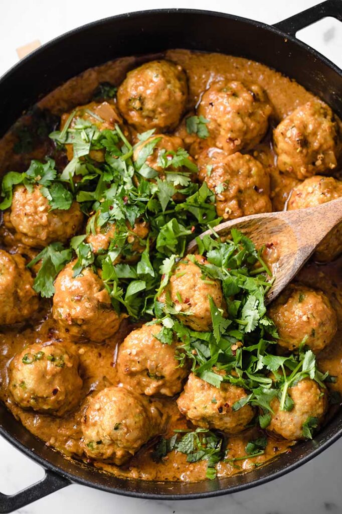 overhead shot of a pan of keto thai coconut curry meatballs atop a marble table