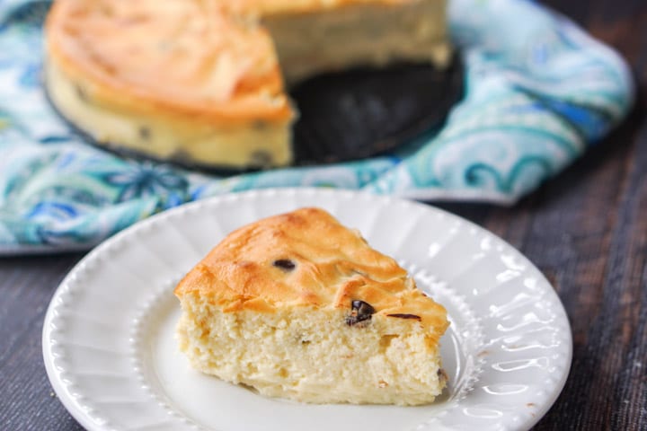 a slice of chocolate chip cheesecake on plate with a whole cake on the background