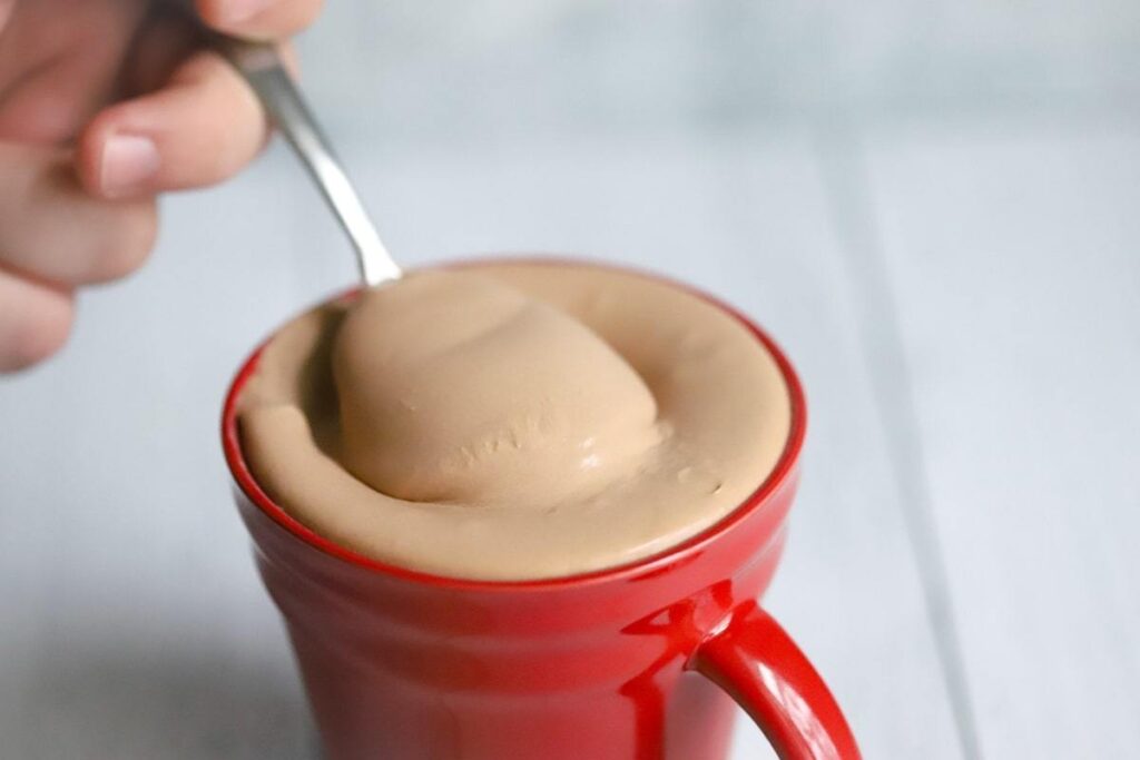 keto fast food recipe - a mug of wendy's copycat keto chocolate frosty being scooped with a spoon atop a marble kitchen coutner