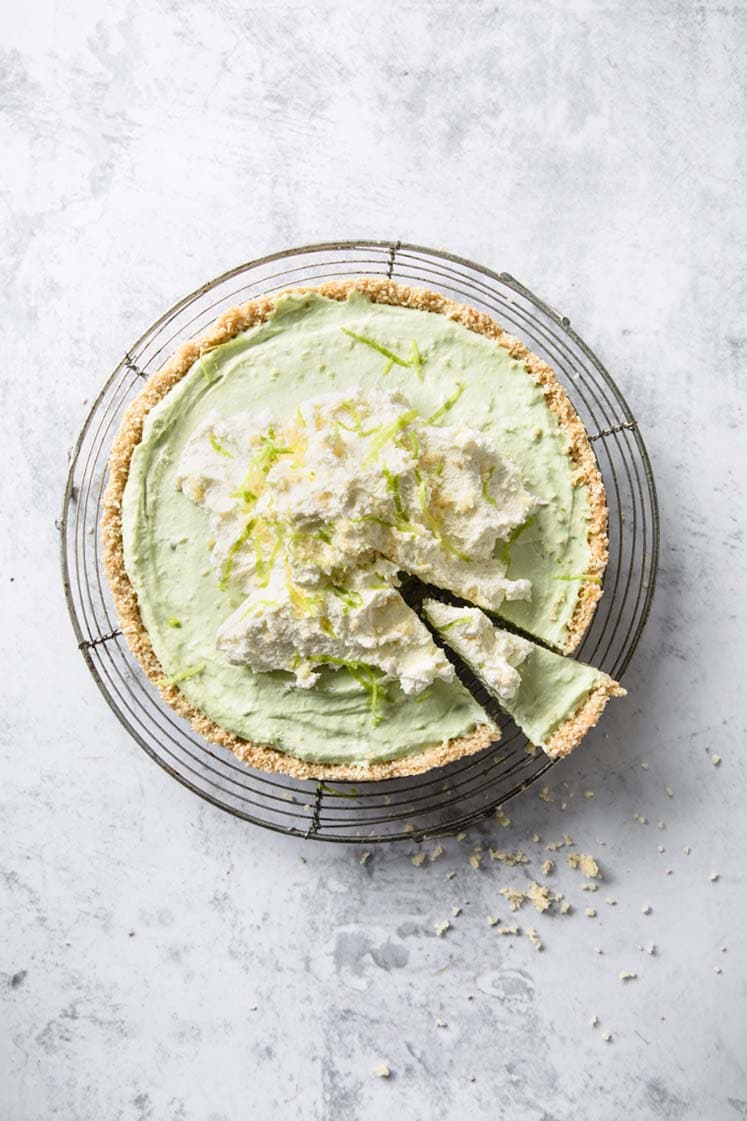 overhead image of a whole Keto Key Lime Pie with a slice slightly taken-out atop a marble kitchen counter