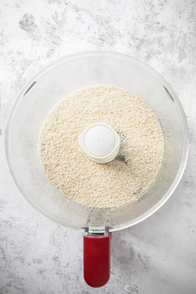 ground shredded coconut and sesame seeds in a food processor atop a marble kitchen counter