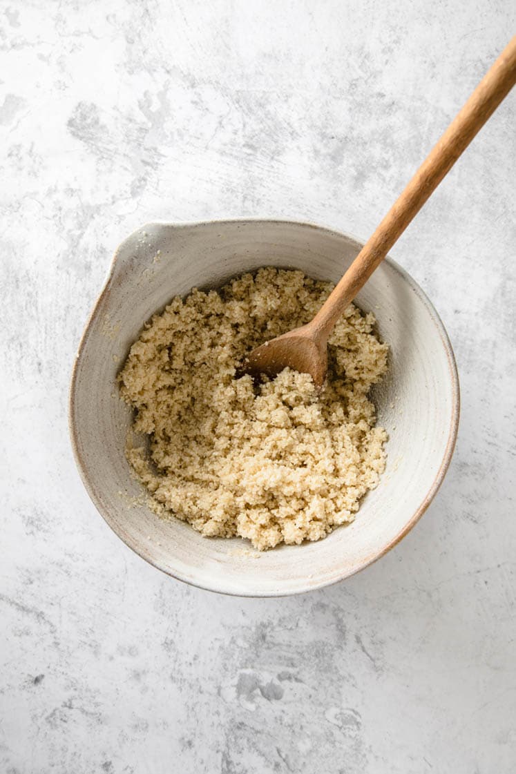 keto key lime pie dough in a bowl with a wooden spoon atop a marble kitchen counter