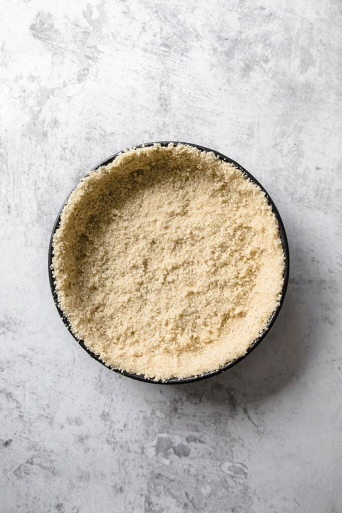 keto key lime pie dough mixture spread into even layer across a springform pan atop a marble kitchen counter