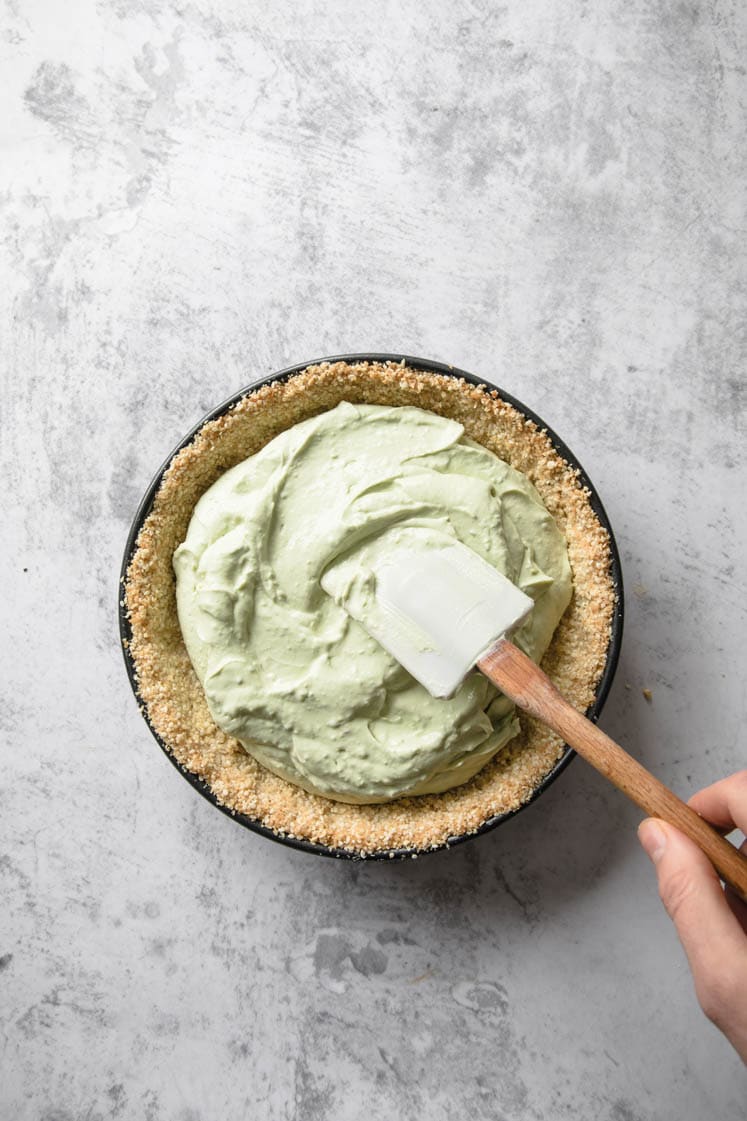 keto key lime pie filling being spooned atop cooled baked crust