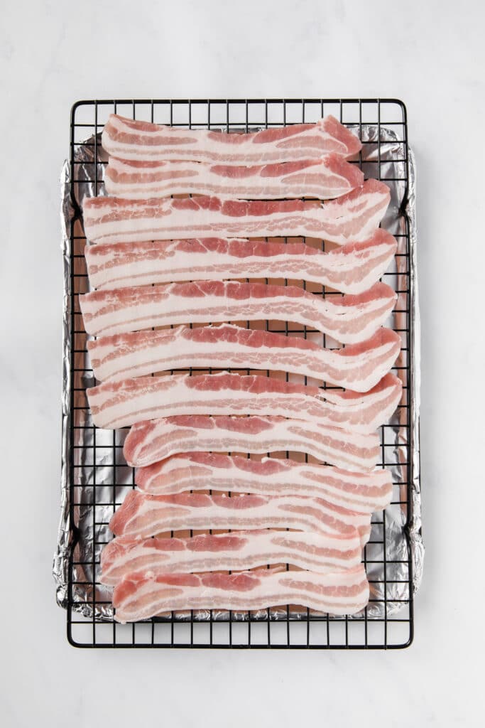 raw bacon laid on top of a baking rack with a foil underneath