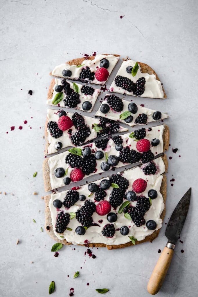 overhead image of fruit pizza that has been sliced into pieces sprinkled with blueberry juice atop a marble kitchen counter