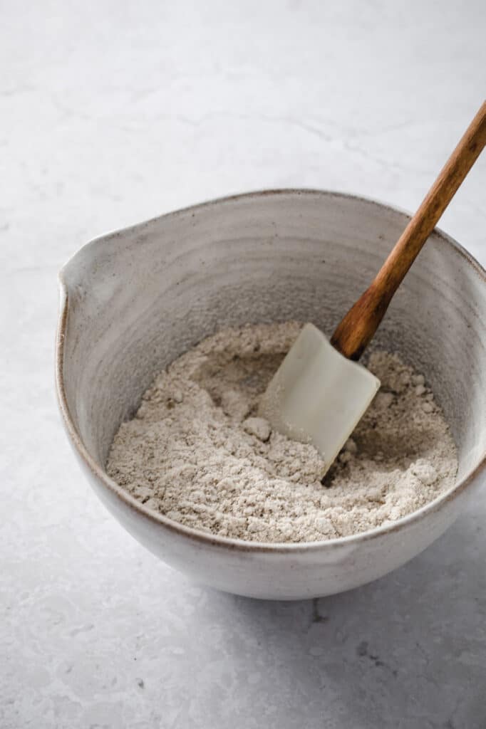 dry crust ingredients mixed in a large mixing bowl using a rubber spatula atop a marble kitchen counter