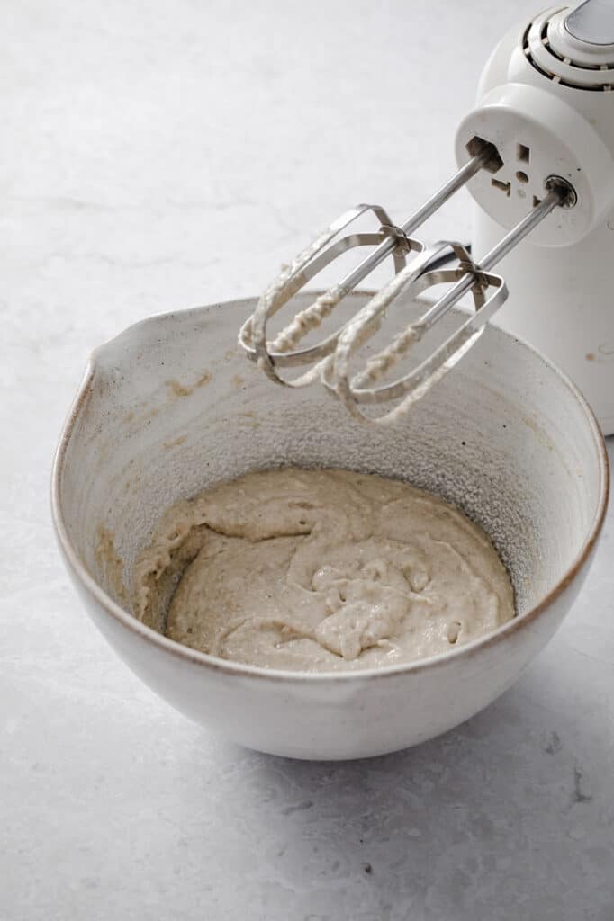 crust mixture on a large mixing bowl mixed with an electric mixer until fully-combined atop a marble kitchen table.